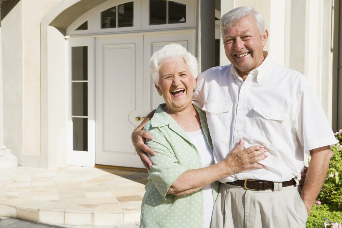senior-couple-embracing-outside-house_StZCrARBs-min